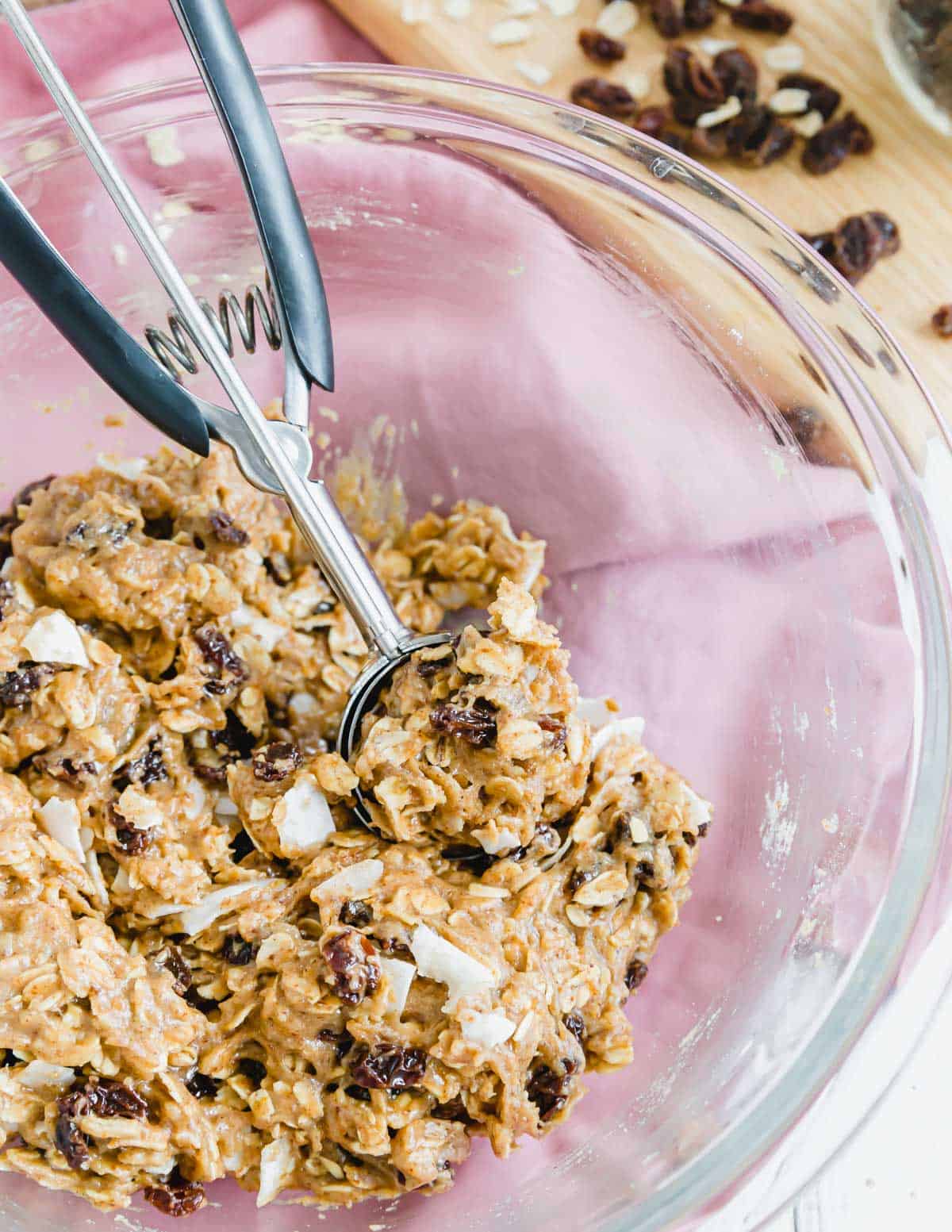 Vegan gluten-free oatmeal raisin cookie dough in a glass bowl with a cookie scoop.