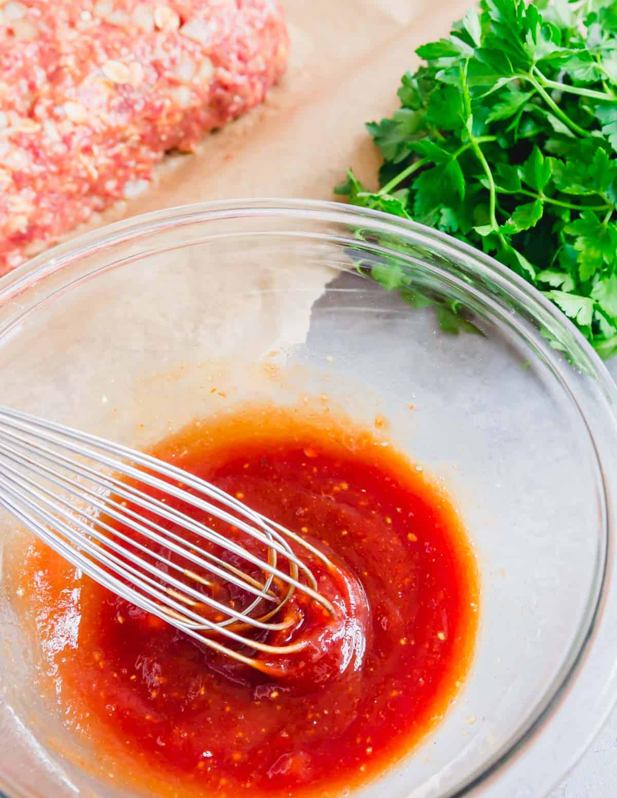 A whisk in a glass bowl with glaze for meatloaf.