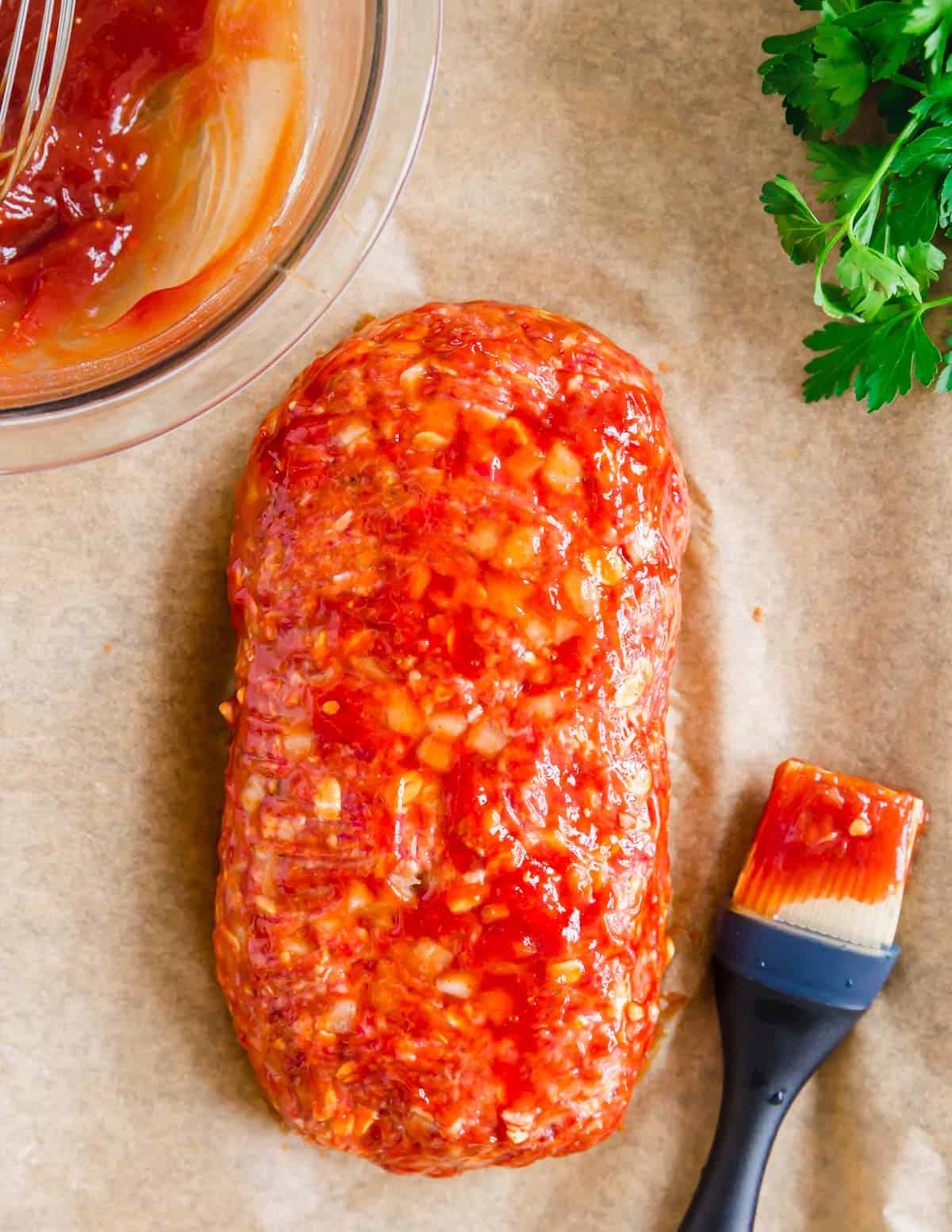 Shaping meatloaf on a baking sheet lined with parchment paper with a brush for glaze on the side.