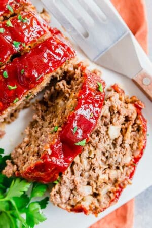 Sliced meatloaf on a white plate with a sweet and tangy glaze and fresh parsley.