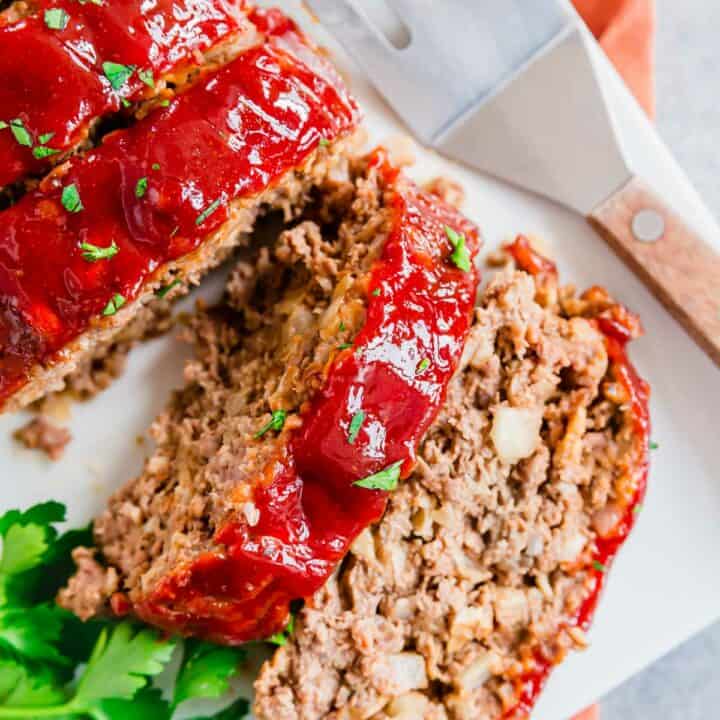 Sliced meatloaf on a white plate with a sweet and tangy glaze and fresh parsley.