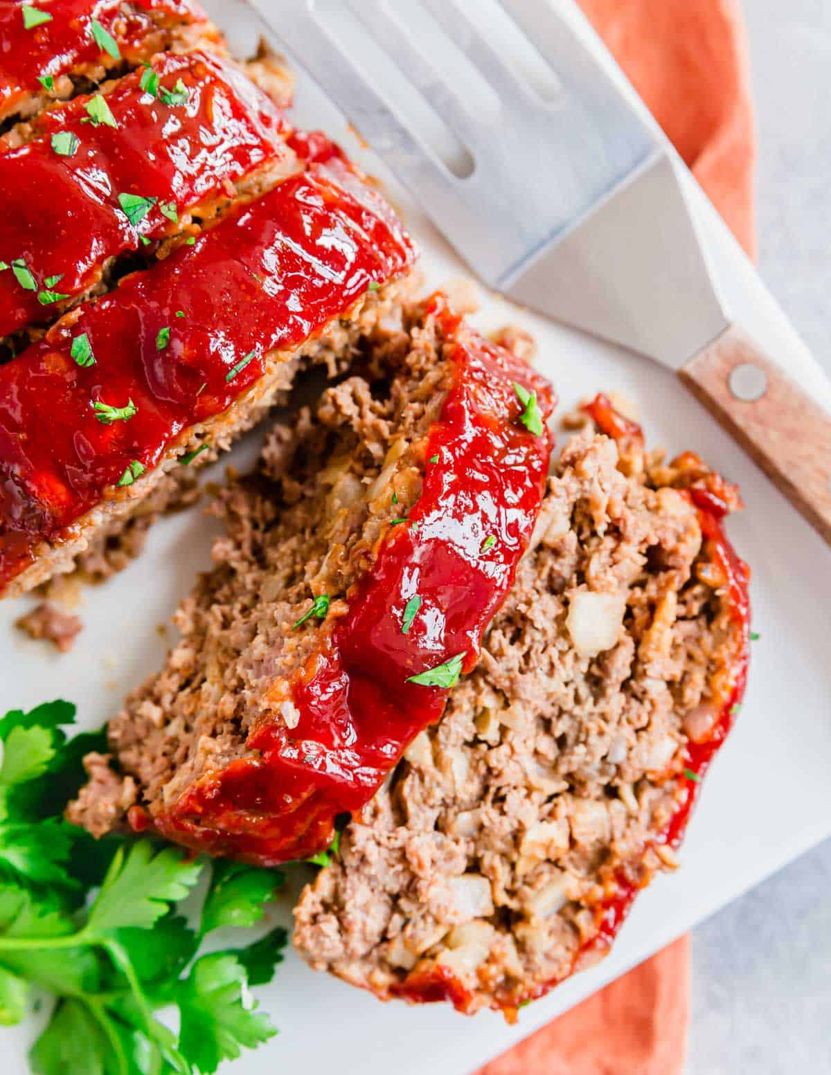 Sliced meatloaf on a white plate with a sweet and tangy glaze and fresh parsley.