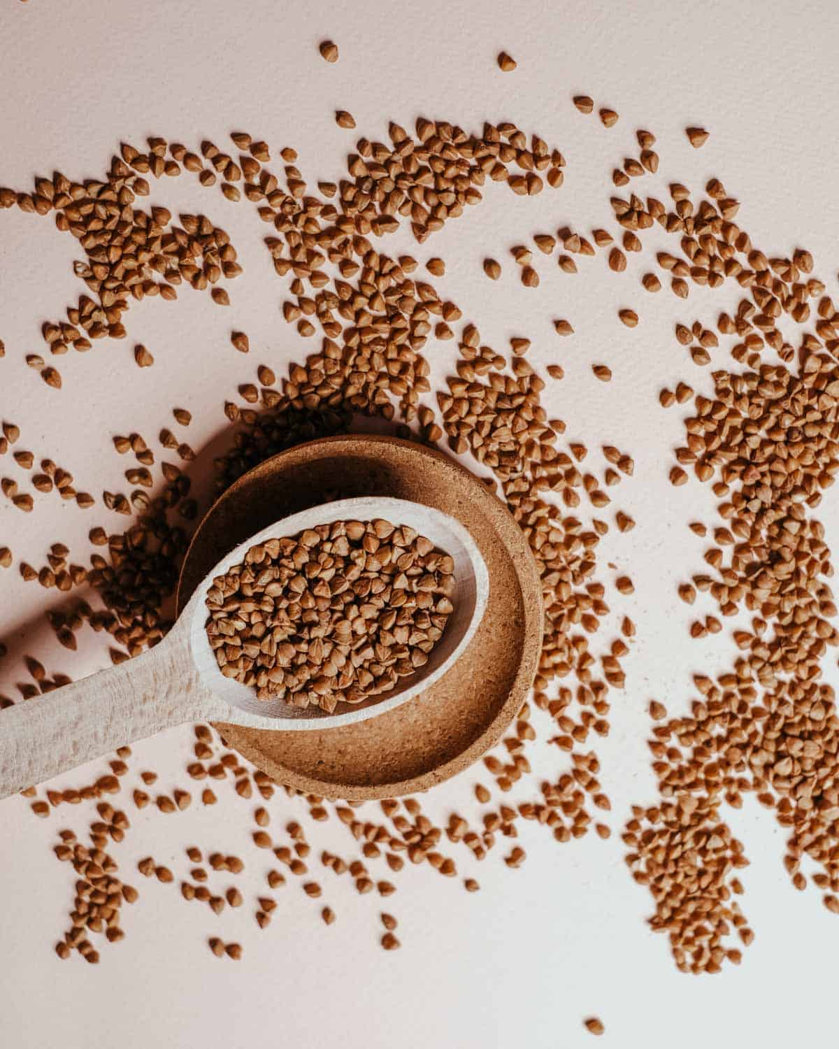 Buckwheat groats scattered on a surface and in a measuring spoon.