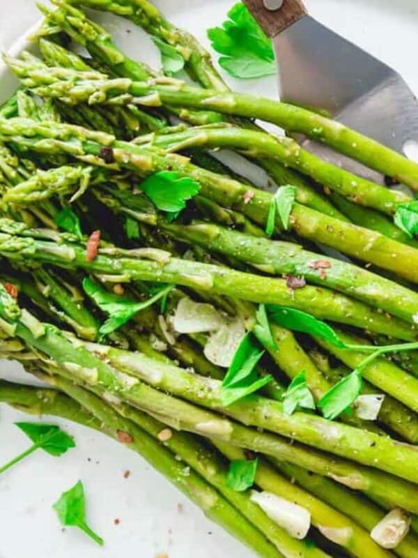 Fresh asparagus garnished with herbs on a white surface.