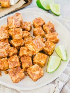 Thai marinated tofu baked until crispy on a plate with lime wedges.