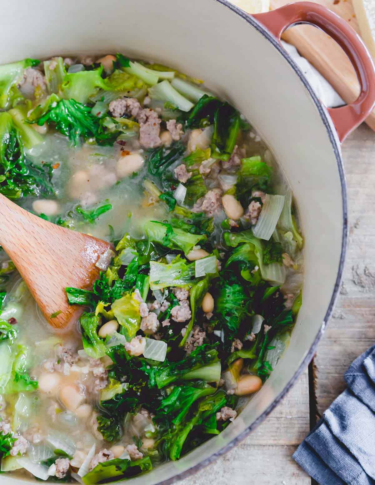 Making escarole soup in a Dutch oven with a wooden spatula.