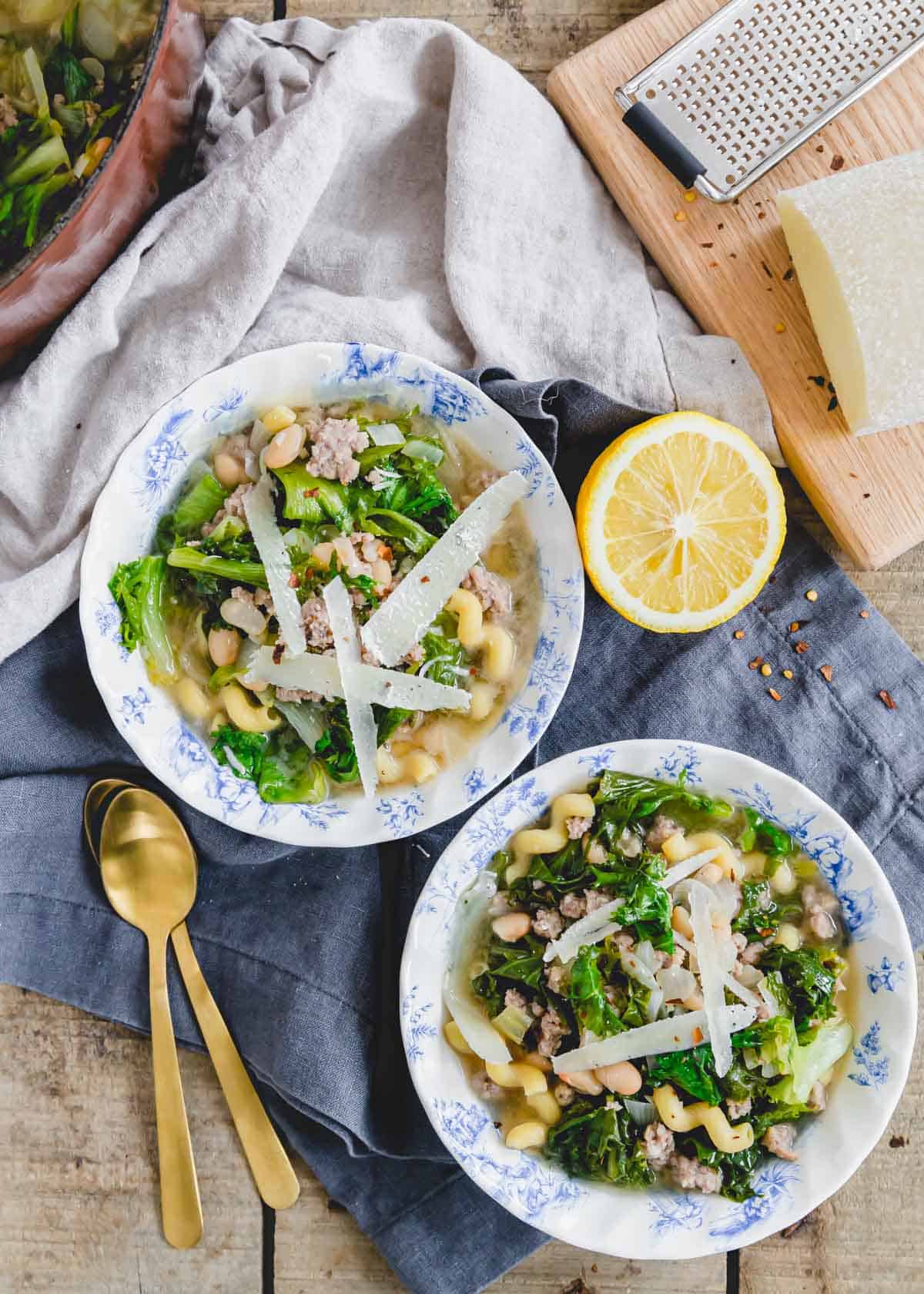 Escarole soup recipe with white beans, ground sausage and pasta in bowls with fresh lemon on the side.