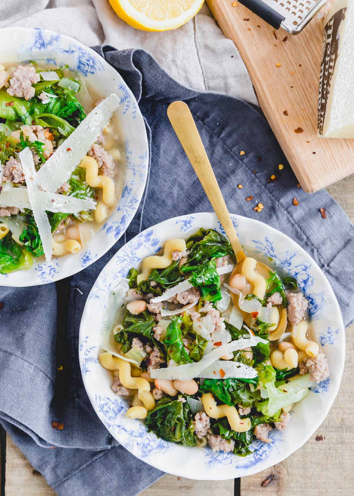 Soup with escarole greens, white beans, pork sausage and gluten-free pasta in bowls with spoons.