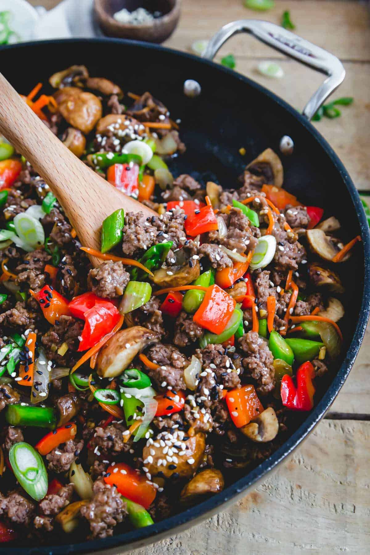 Ground beef stir fry in a skillet with a wooden spoon.