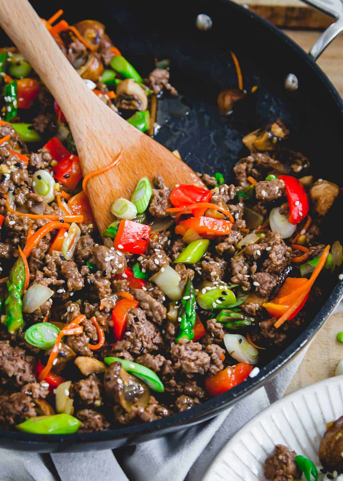 Ground beef with vegetables coated in a homemade stir fry sauce in a pan with wooden spatula.