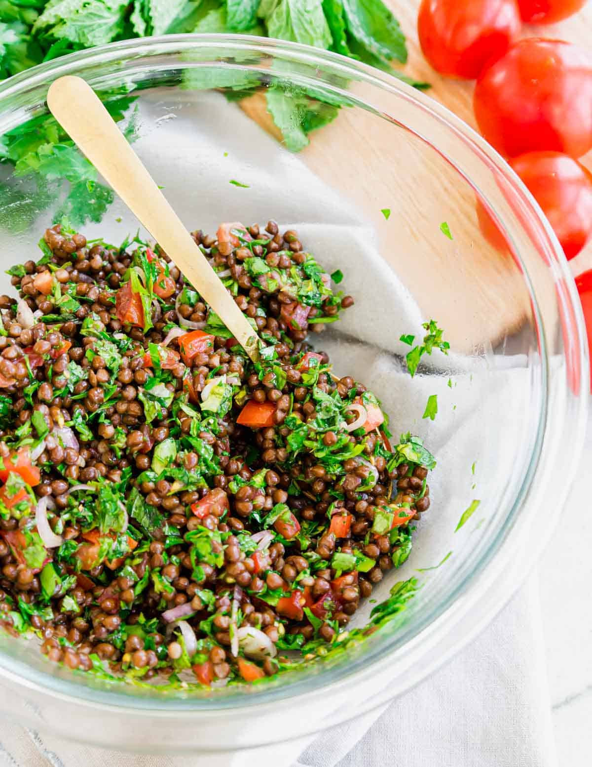 Mixing lentil tabbouleh together in a glass bowl with a spoon.