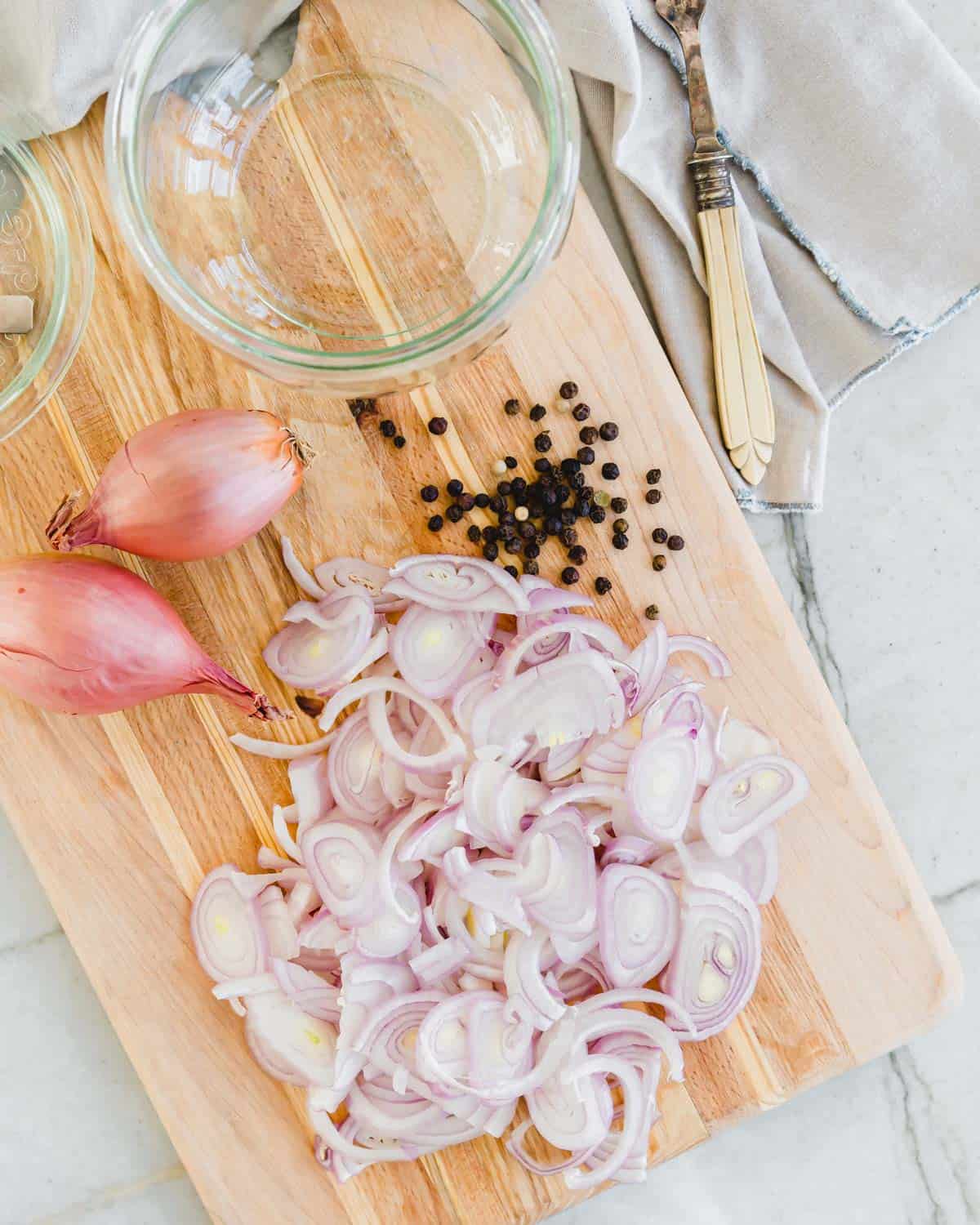 Sliced shallots and peppercorns on a cutting board.