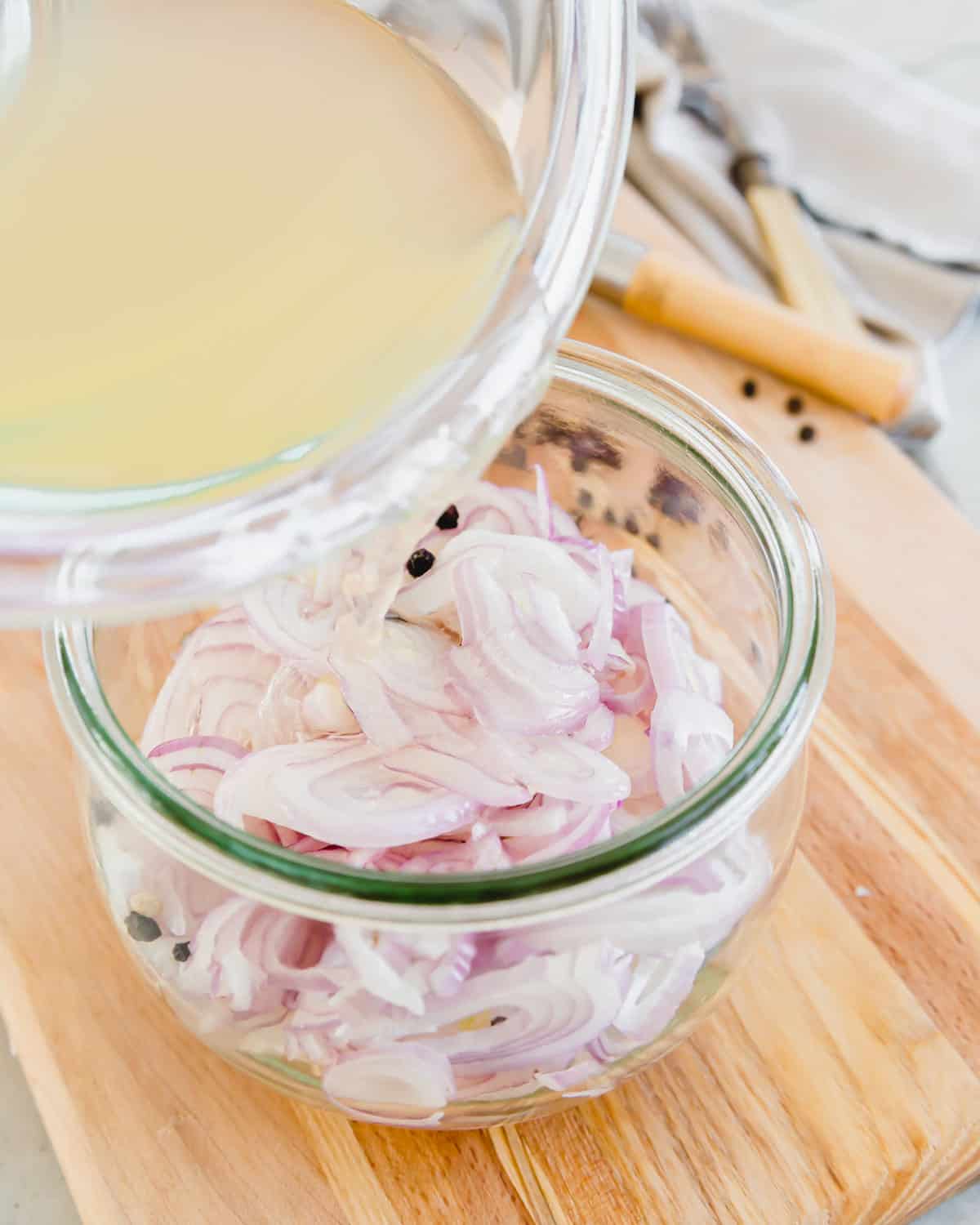 Pouring pickling brine over shallots in a glass jar.