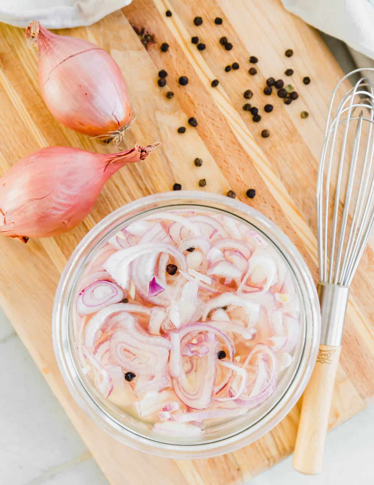 Quick pickled shallots in a glass jar with peppercorns.