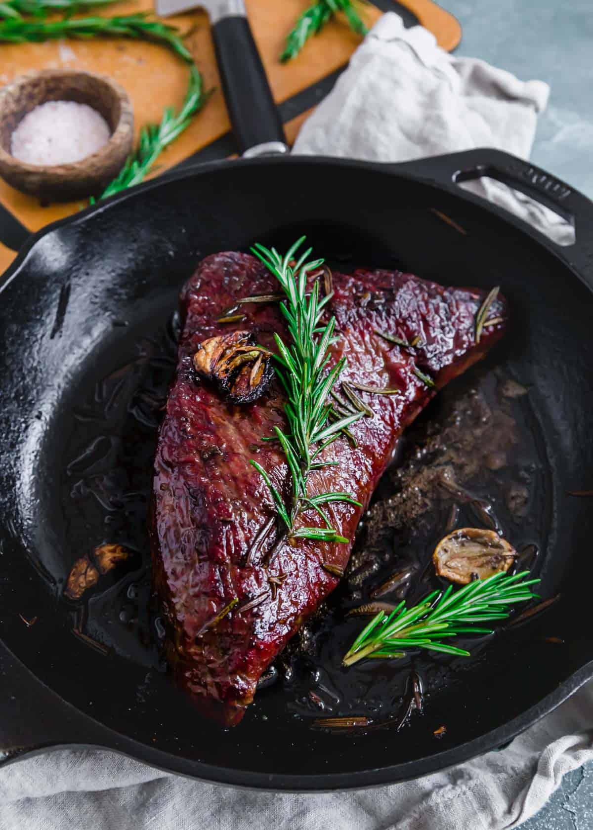 Tri tip in a cast iron skillet with rosemary sprigs and garlic.