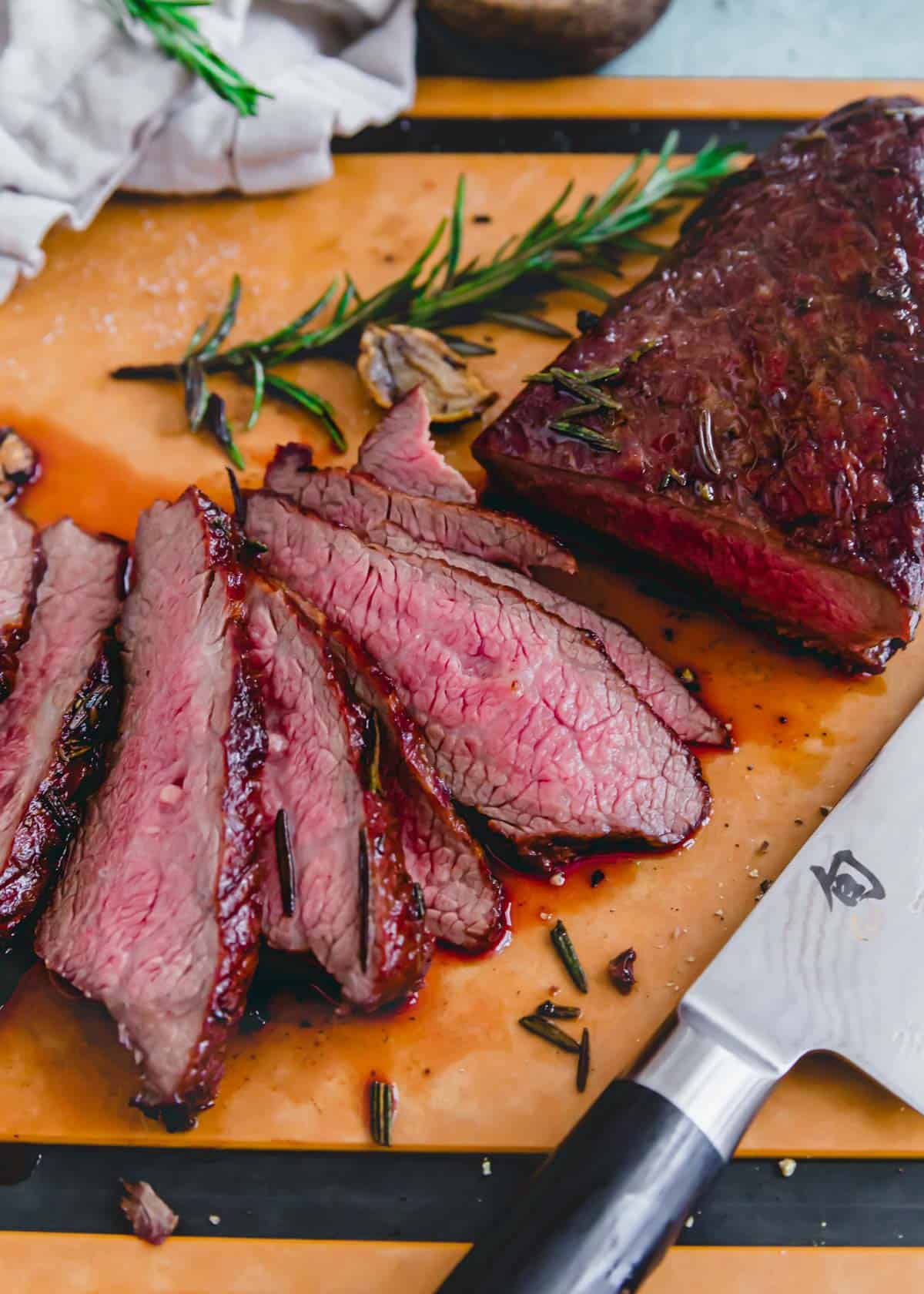 Tri tip steak cut against the grain in thin slices on a cutting board.