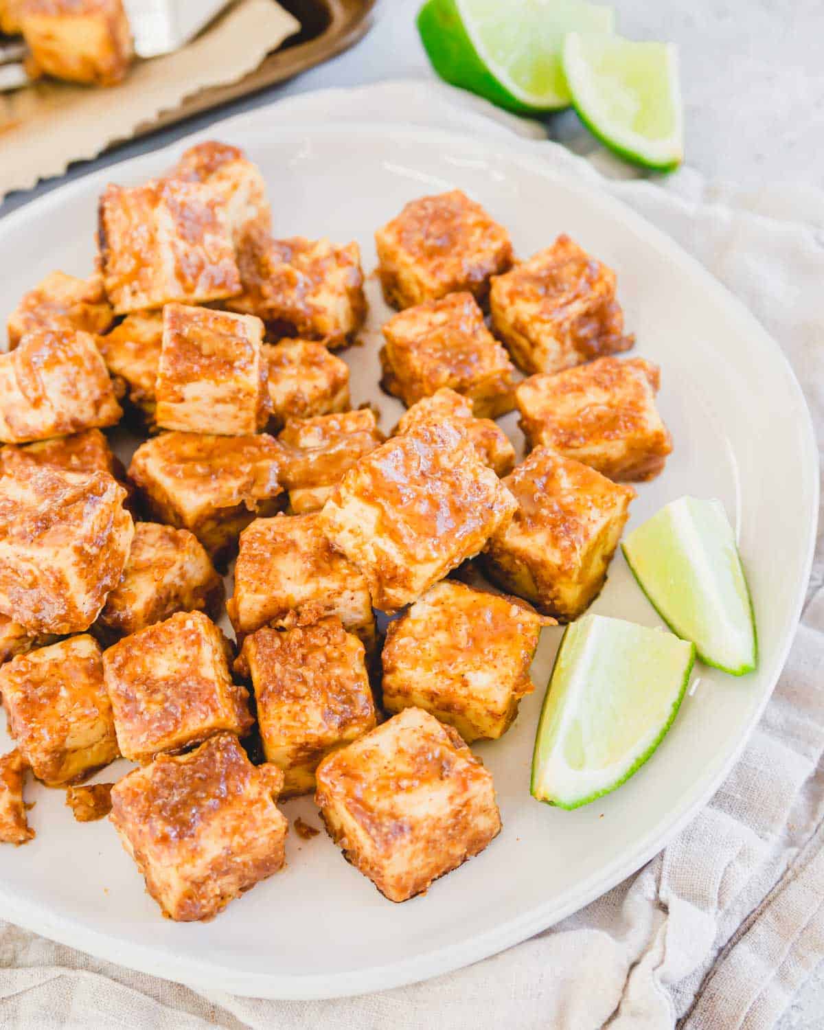 Thai marinated tofu baked until crispy on a plate with lime wedges.