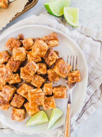 Marinated tofu on a plate with a fork and lime wedges.