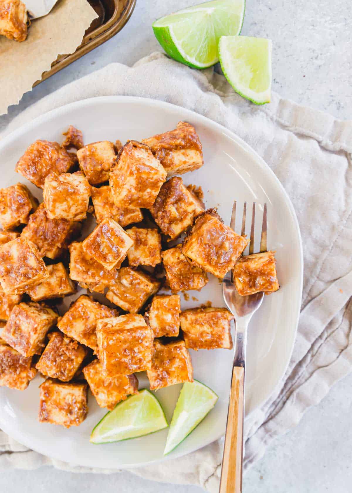 Marinated tofu on a plate with a fork and lime wedges.