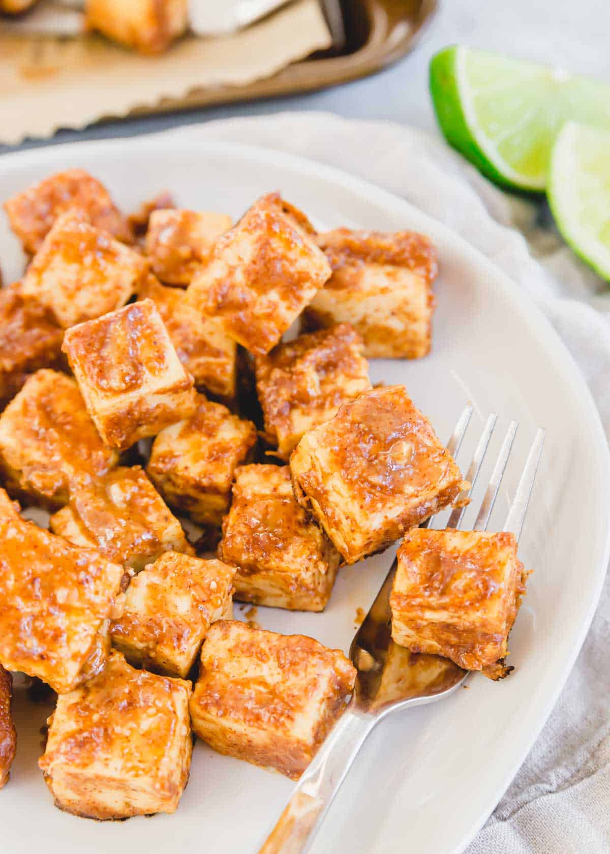 The best tofu marinade made of almond butter, lime juice, garlic, ginger and soy baked until crispy on a white plate with a fork.