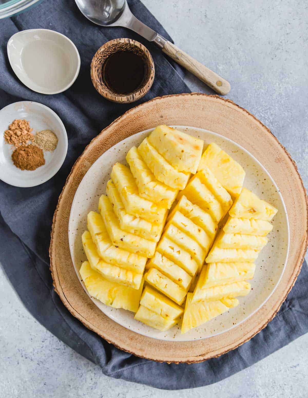 Sliced pineapple on a plate with cinnamon spices, maple syrup and coconut oil in bowls to the side.