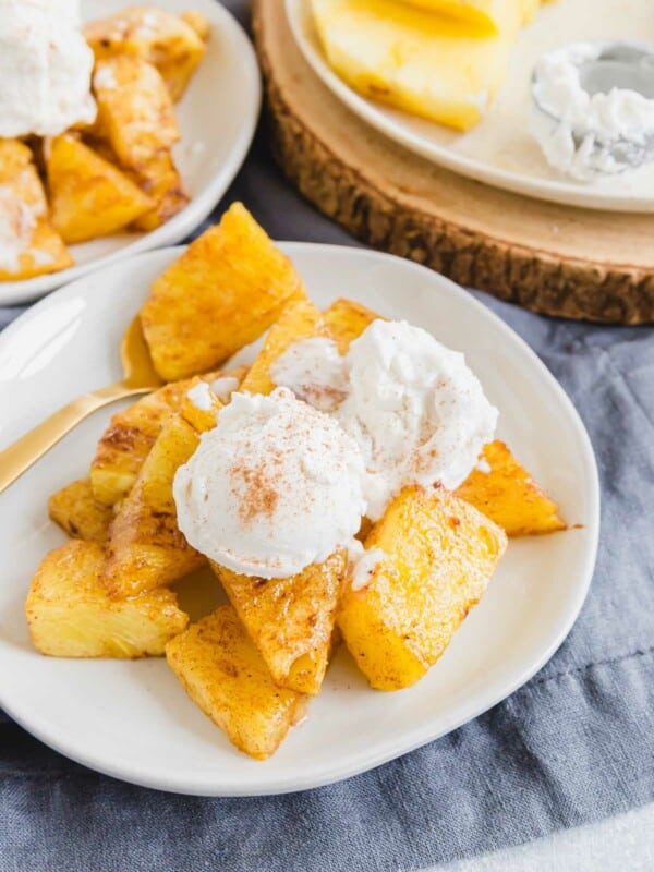 Air fryer pineapple with vanilla ice cream and dusting of cinnamon on a white plate.