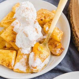 Close up of caramelized air fryer pineapple on a plate with ice cream and cinnamon dusting.