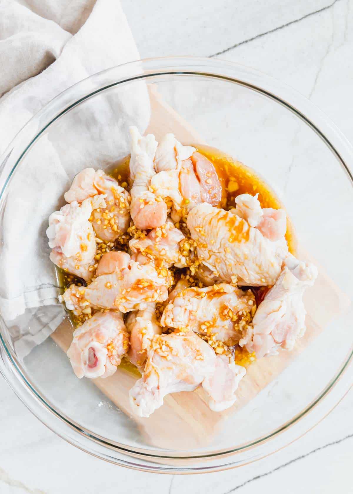 Raw chicken wings marinating in a glass bowl.