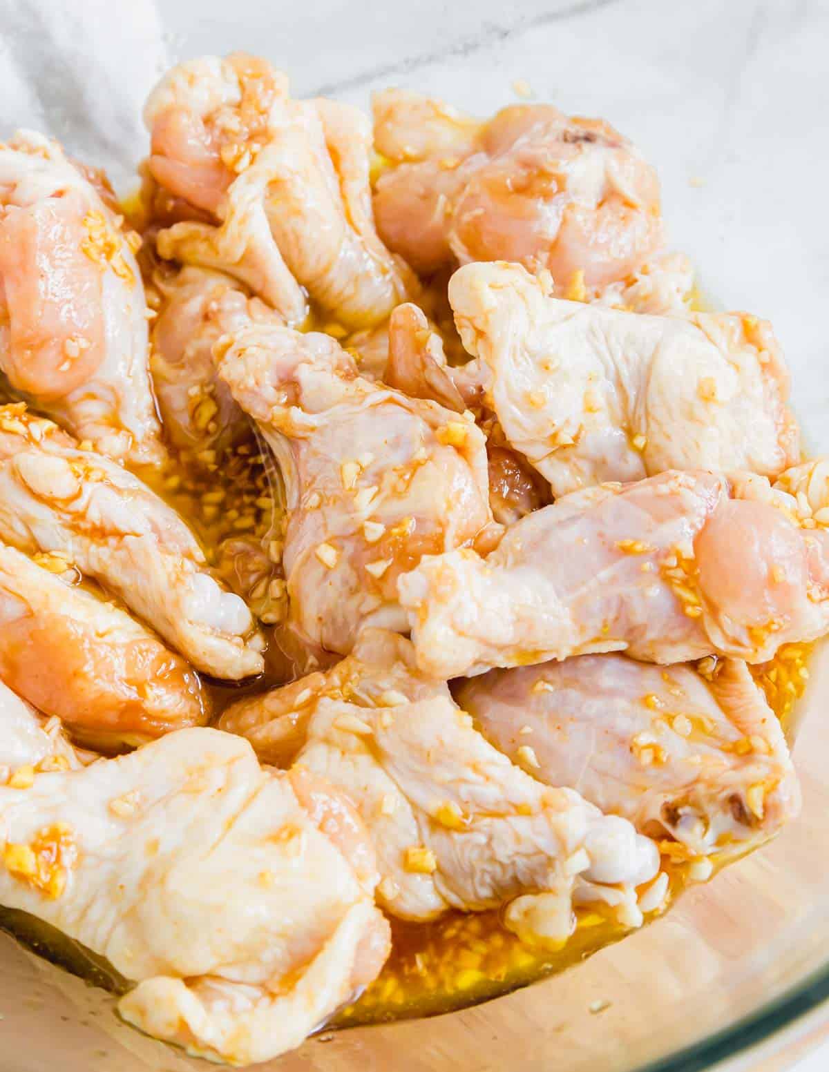 Close up of chicken wings marinating in a glass bowl.