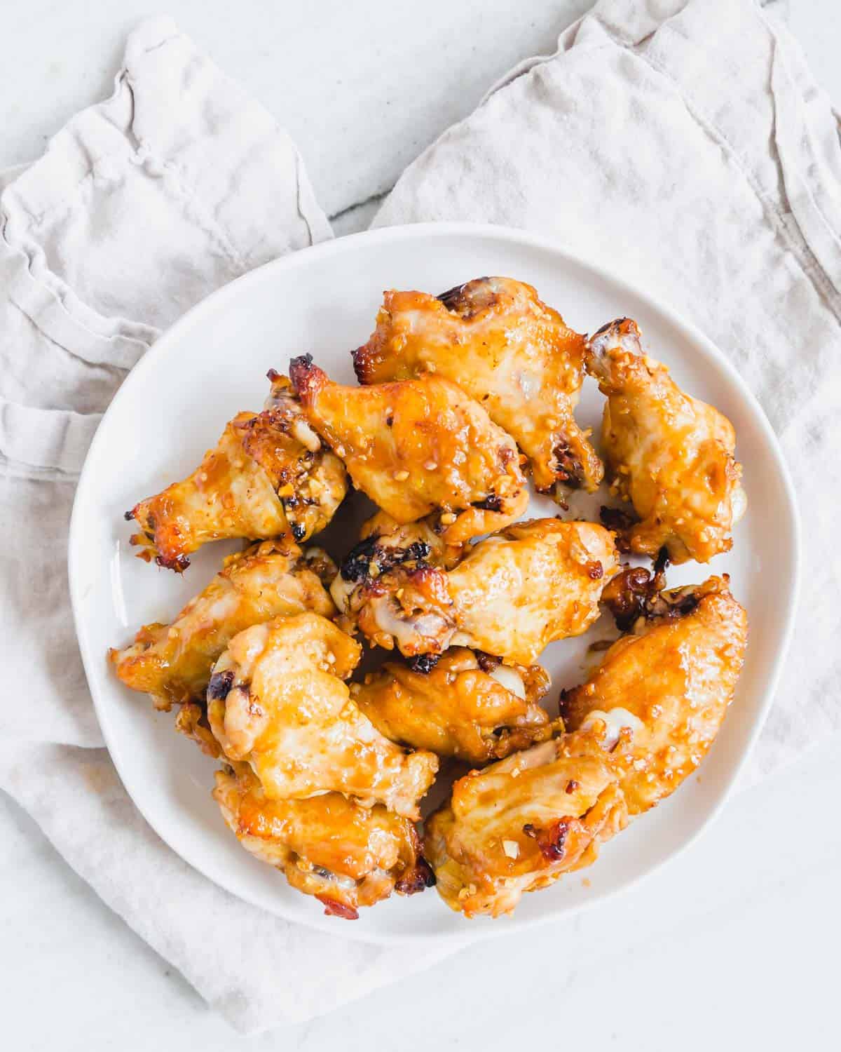 Easy marinated baked chicken wings on a plate with a neutral colored kitchen towel.