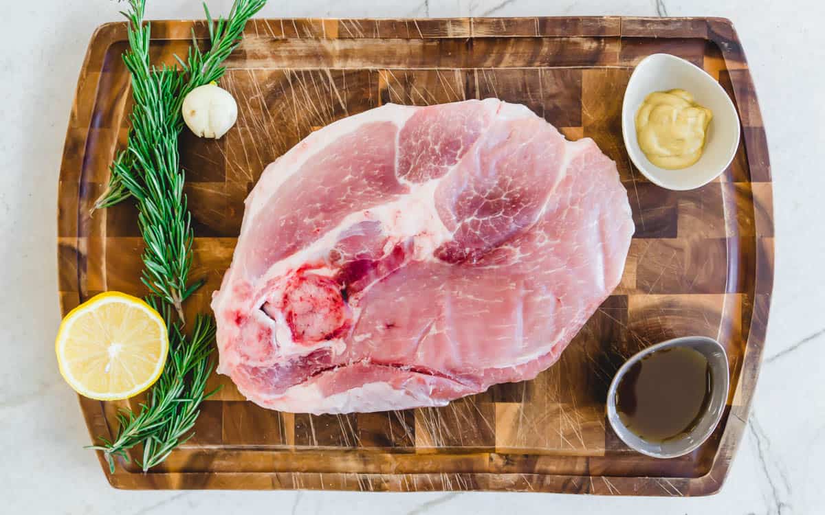Fresh ham steak on a cutting board with ingredients to make a glaze.