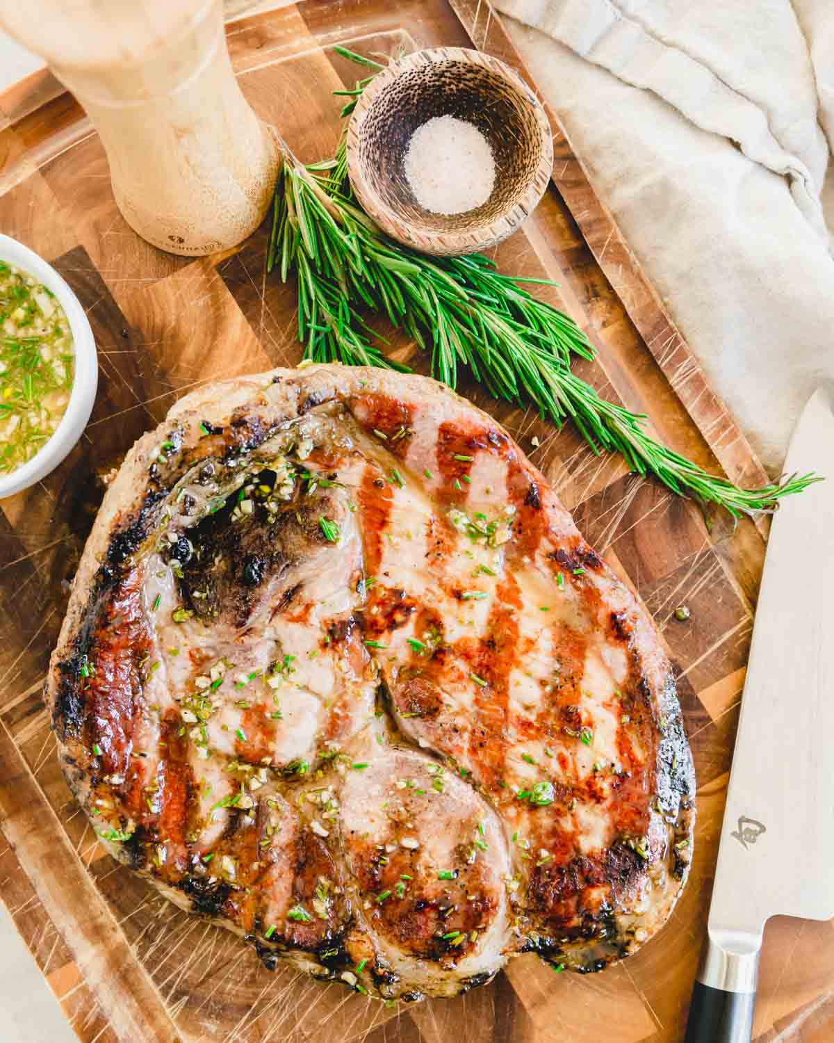 Grilled ham steak with rosemary maple dijon glaze on a cutting board with rosemary, salt and pepper.