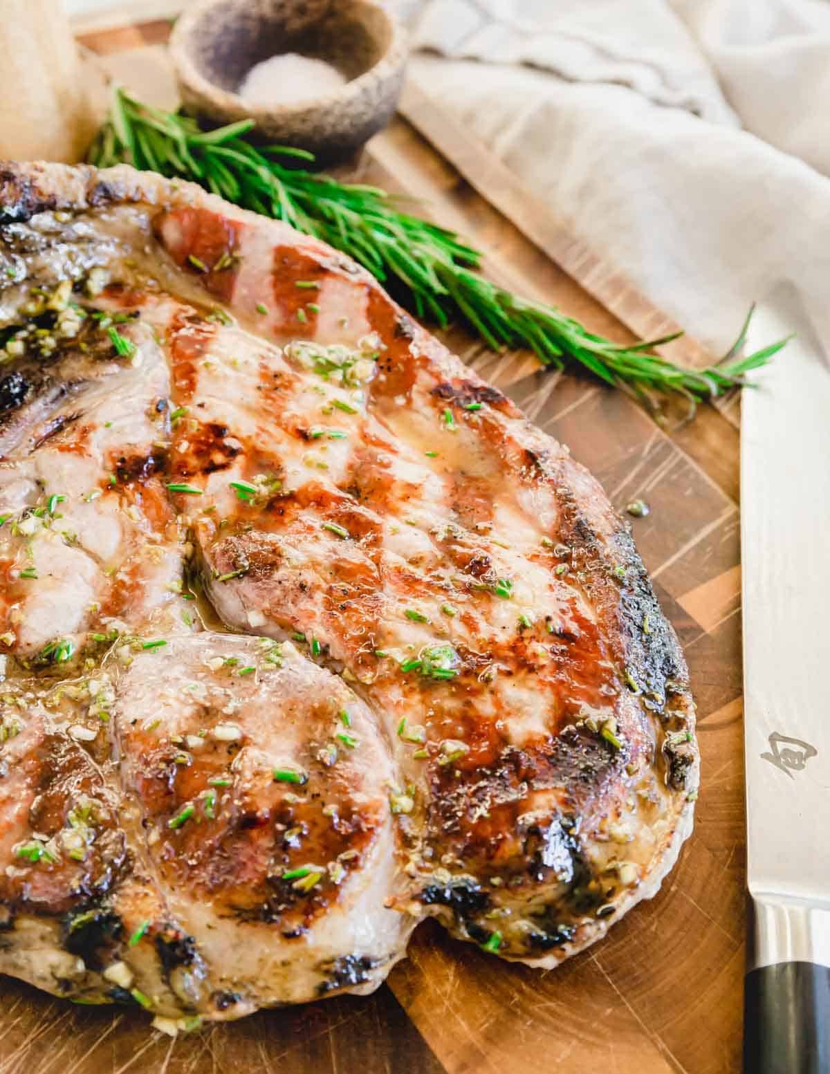 Ham steak fresh off the grill on a cutting board with a sharp chef's knife.