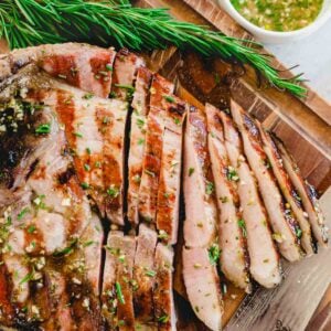 Sliced grilled ham steak on a cutting board with fresh rosemary sprigs and knife.