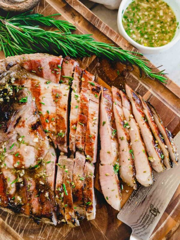 Sliced grilled ham steak on a cutting board with fresh rosemary sprigs and knife.