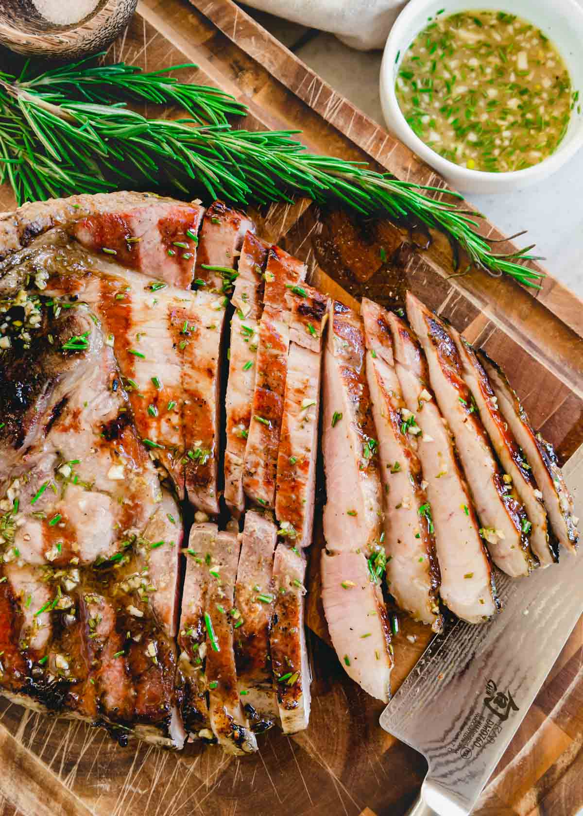 Sliced grilled ham steak on a cutting board with fresh rosemary sprigs and knife.