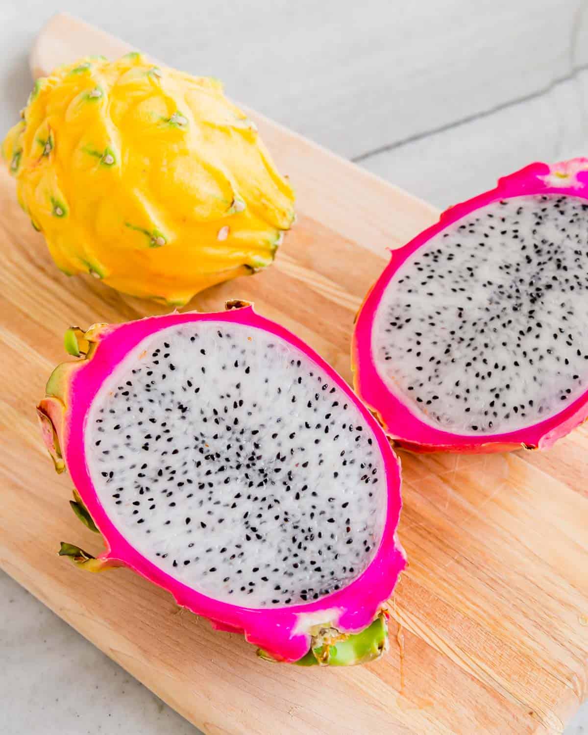 Pink dragonfruit with white flesh cut in half on a cutting board.