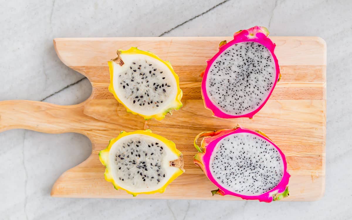 Yellow and pink dragonfruit sliced in half on a cutting board.