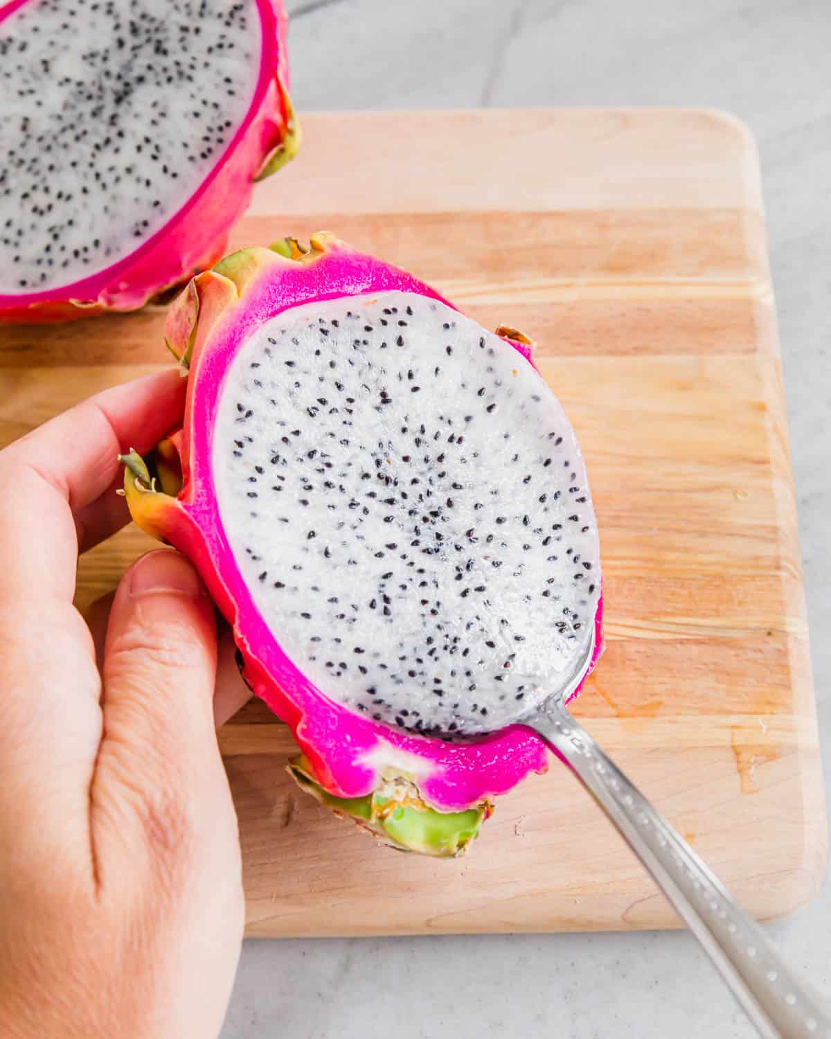 Scooping dragonfruit out of the peel with a spoon.