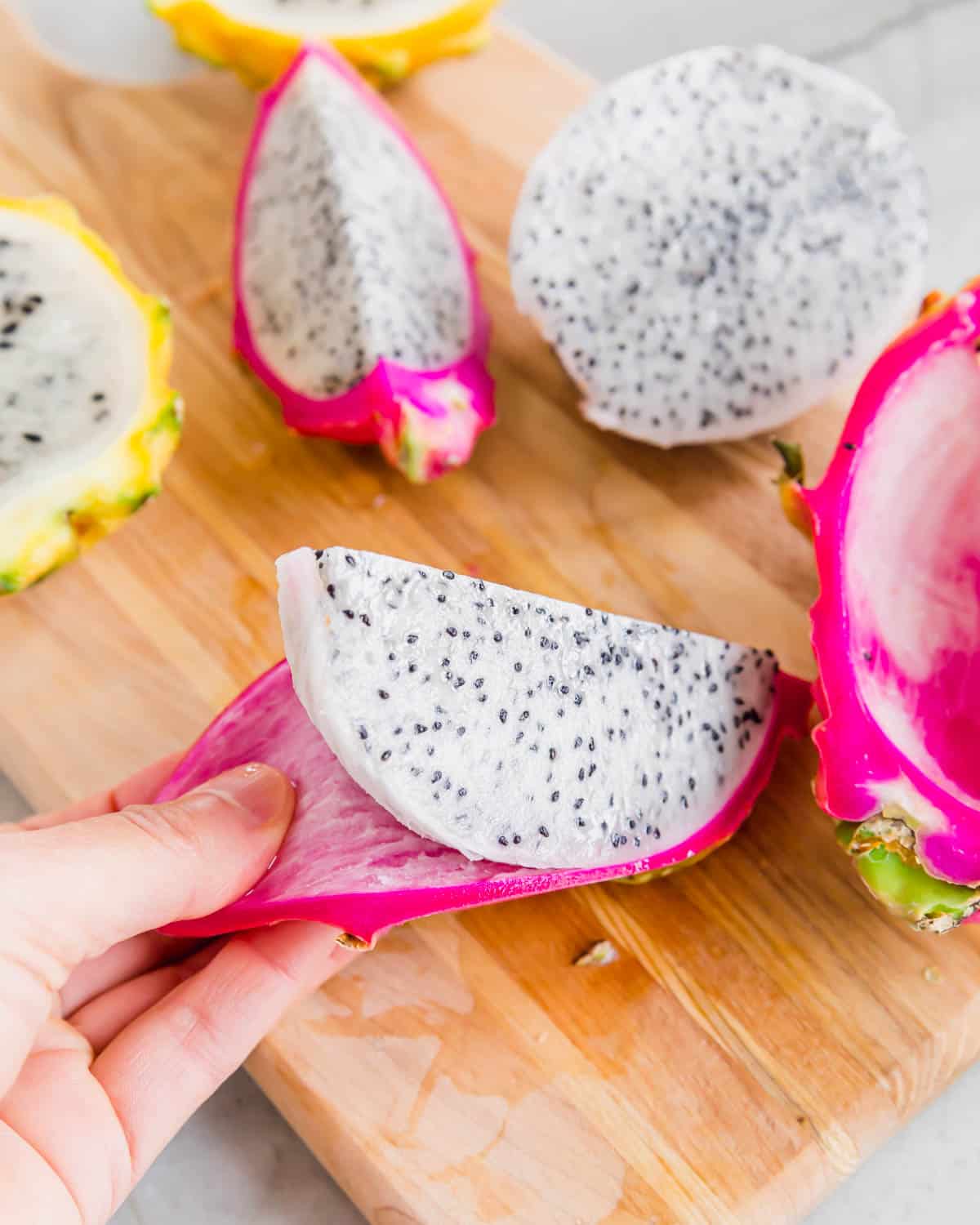 Hands peeling dragonfruit flesh off the skin.