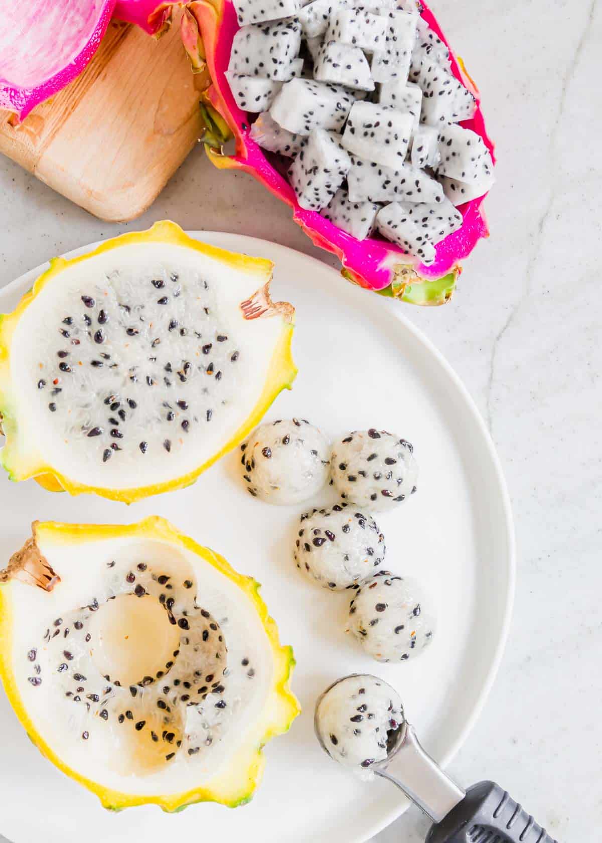 Using a melon baller to scoop out balls of dragonfruit on a white plate.