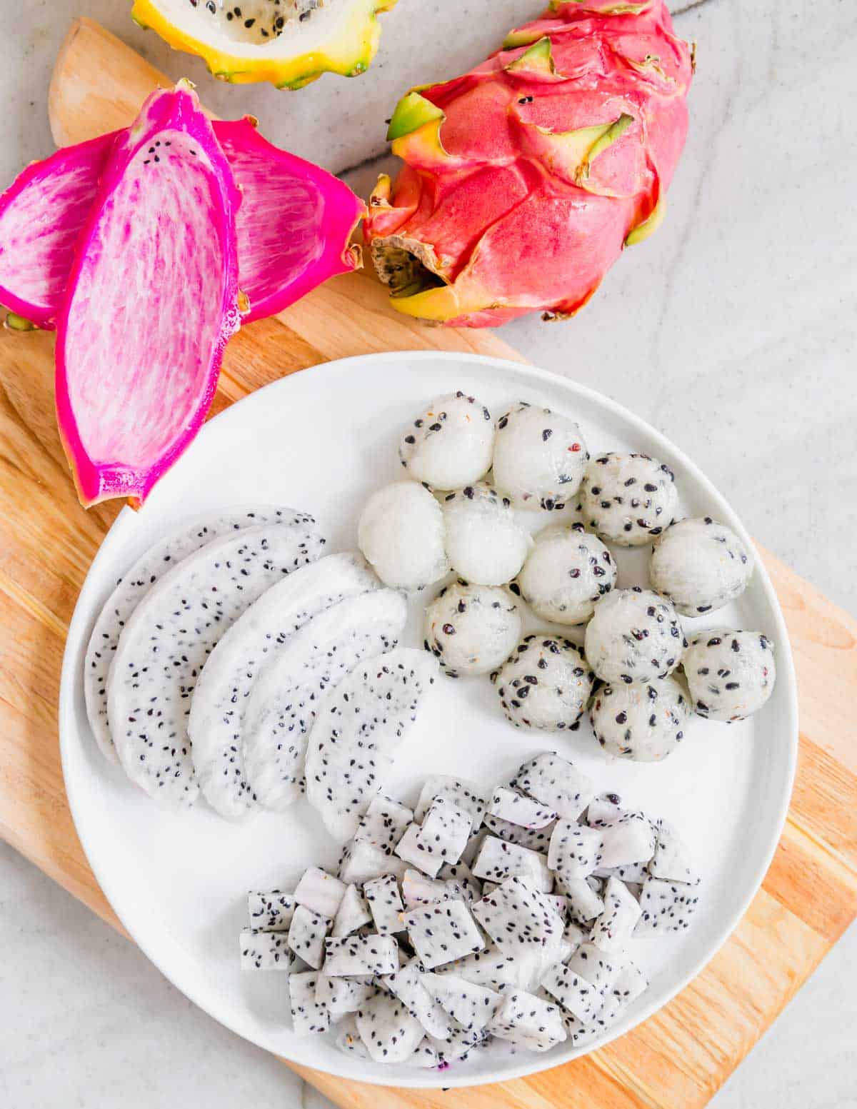 Dragonfruit cut into slices, balls and cubes on a plate.