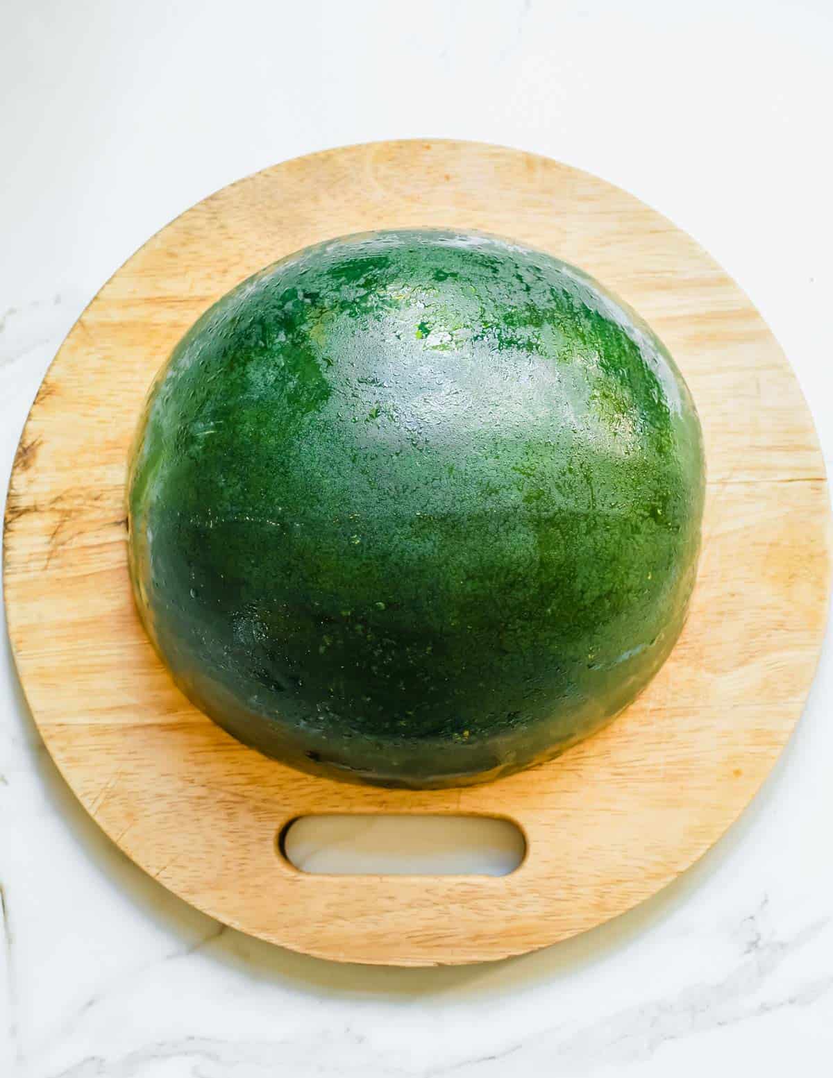 Watermelon cut in half face down on a cutting board.