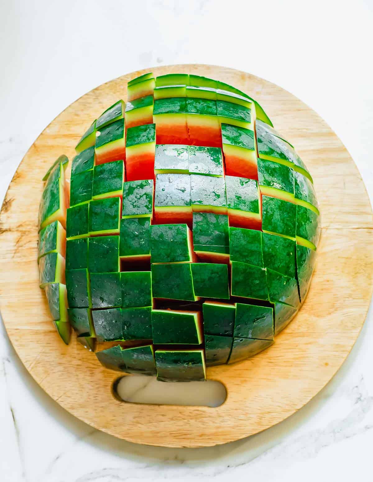 Half a watermelon cut side down on cutting board sliced into pieces.