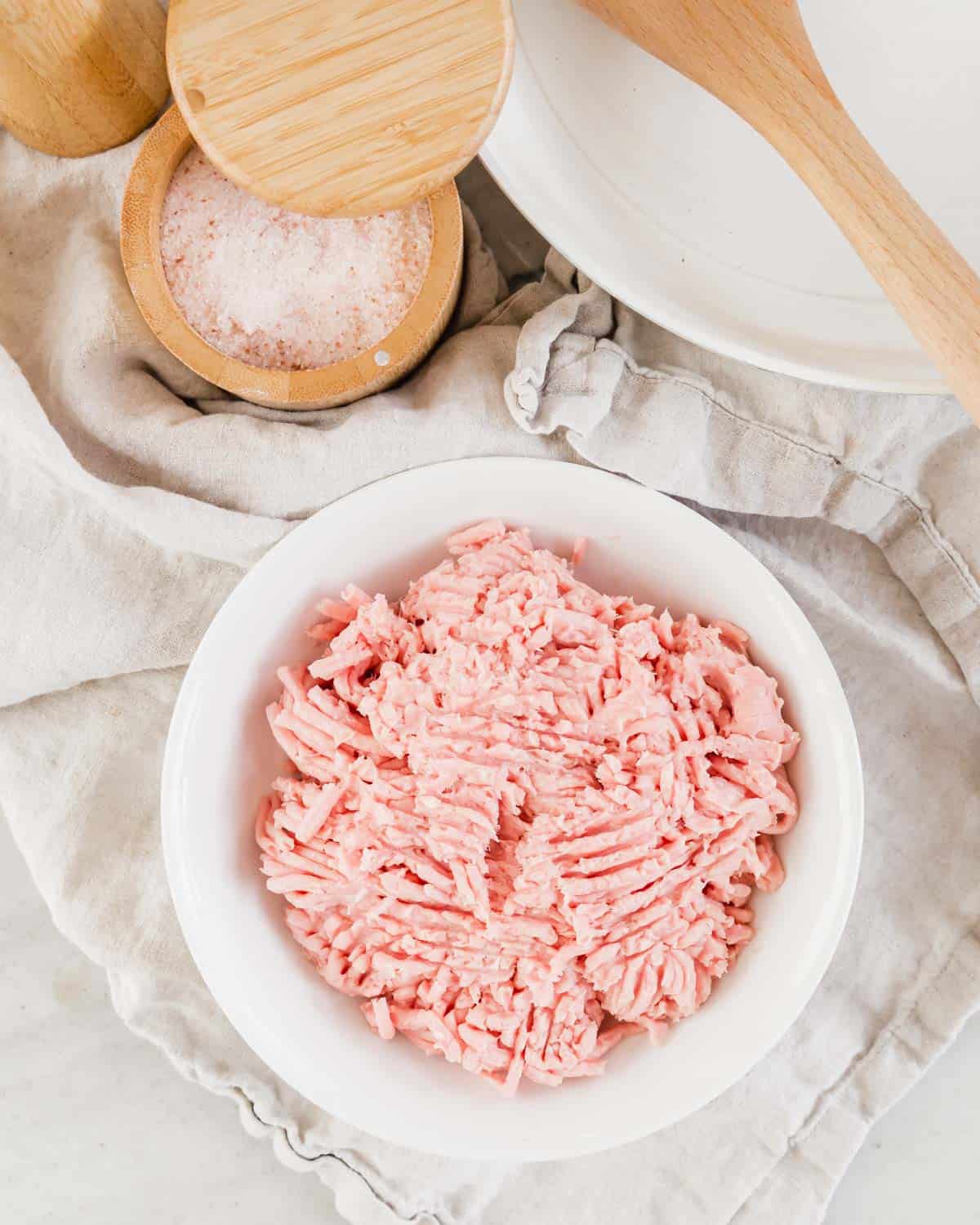 Ground turkey in a white bowl with salt and pepper next to it.