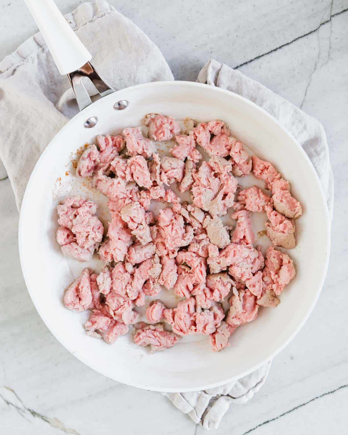 Partially cooked ground turkey in a white skillet.