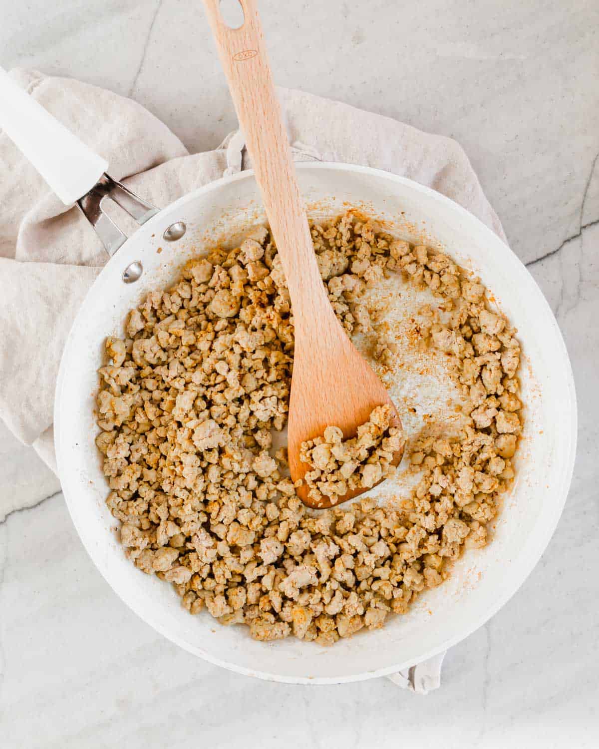 Seasoned ground turkey meat in a skillet with a wooden spatula.