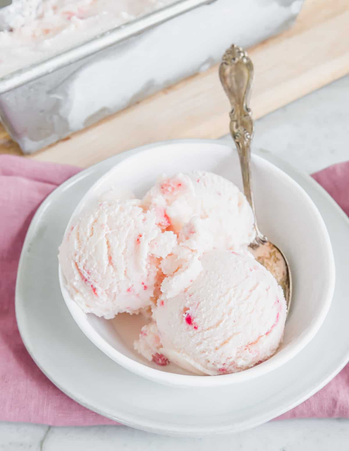 Strawberry vanilla kefir ice cream in a white bowl with a spoon.