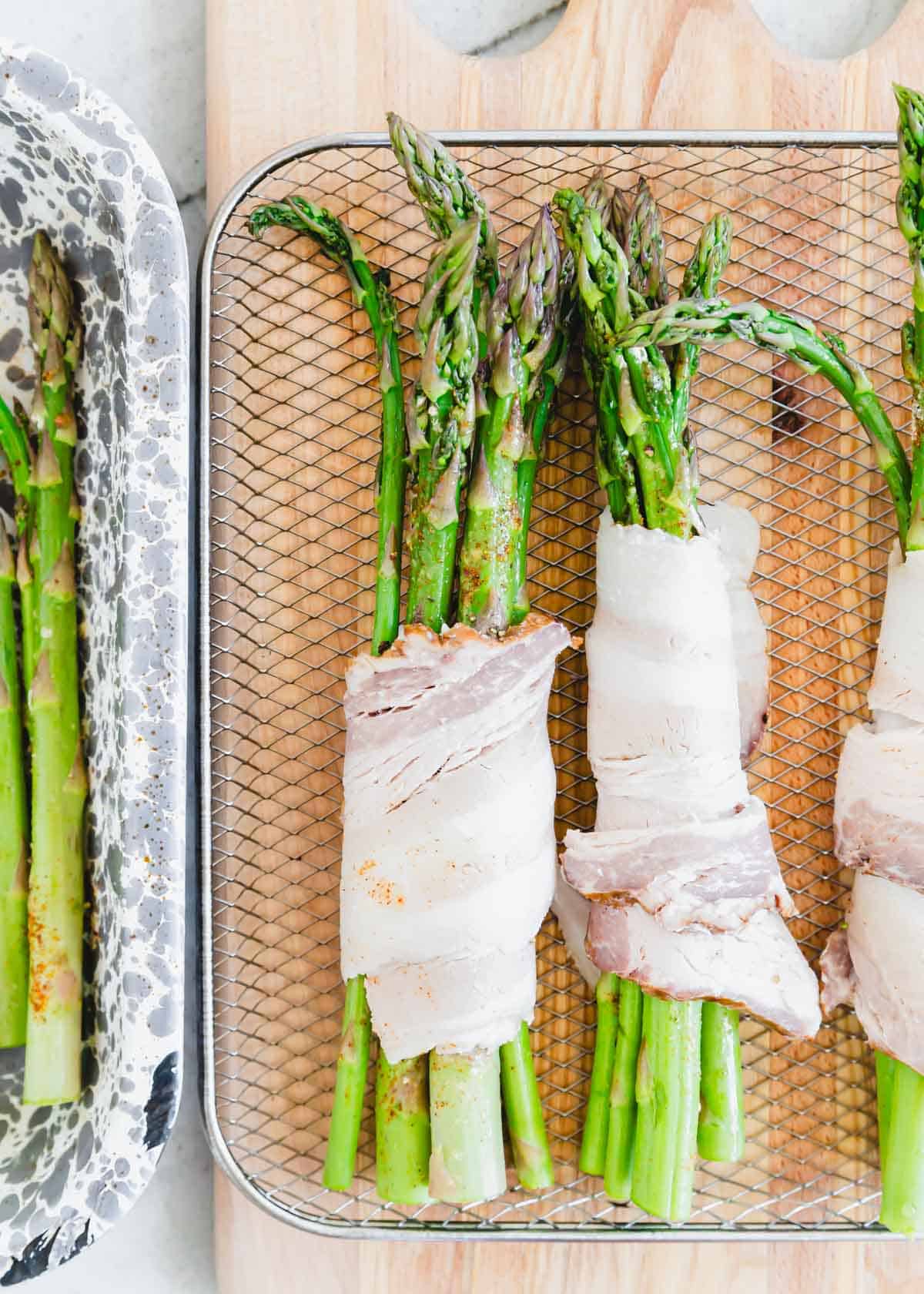 Asparagus bundles wrapped in raw bacon on a wire air fryer rack.