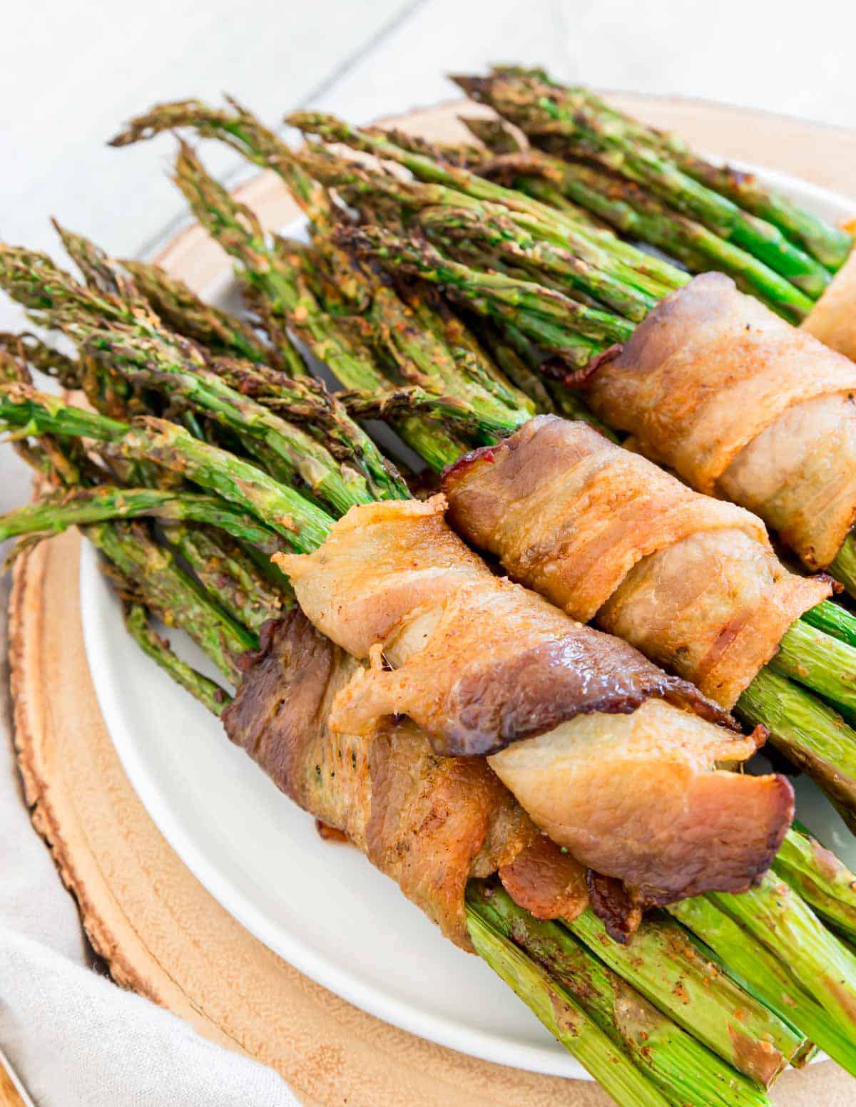 Air fryer asparagus wrapped bacon bundles stacked on a white plate.